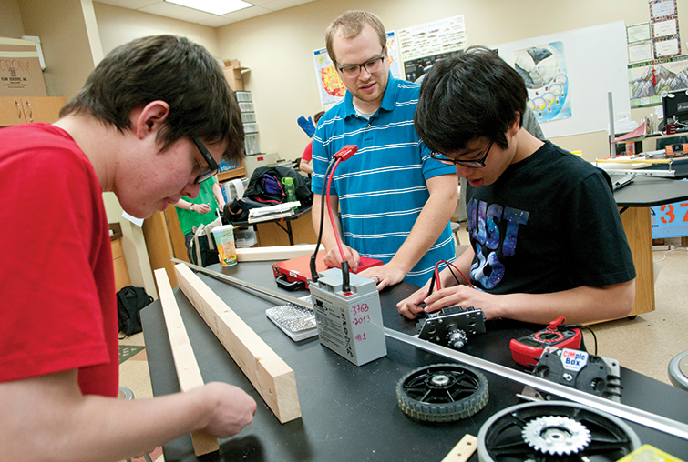 Augsburg alumnus Dan Forseth works with two students in a classroom